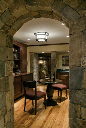 A simple ceiling fixture featuring a simple form and subtle old world details adds a transitional design counterpoint to this cellar's natural stone masonry and rich mahogany.