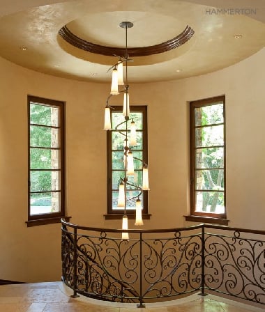 A spiraling fixture of sienna-tinted blown glass echoes the scrollwork in the surrounding stairway railing. Interiors by Alison Whittaker Design Inc.