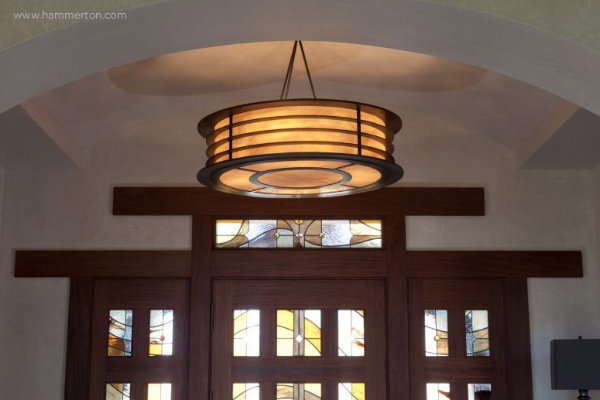 A striking ceiling fixture crafted with glass and steel beautifully complements the warm wood tones of the stained glass and mahogany woodwork in the home's front entryway.