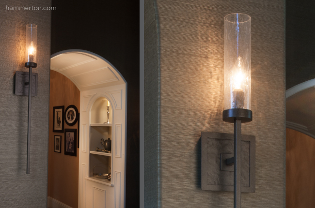 A simple, elegant wall sconce featuring a single candlestick light with a cylindrical clear glass diffuser
