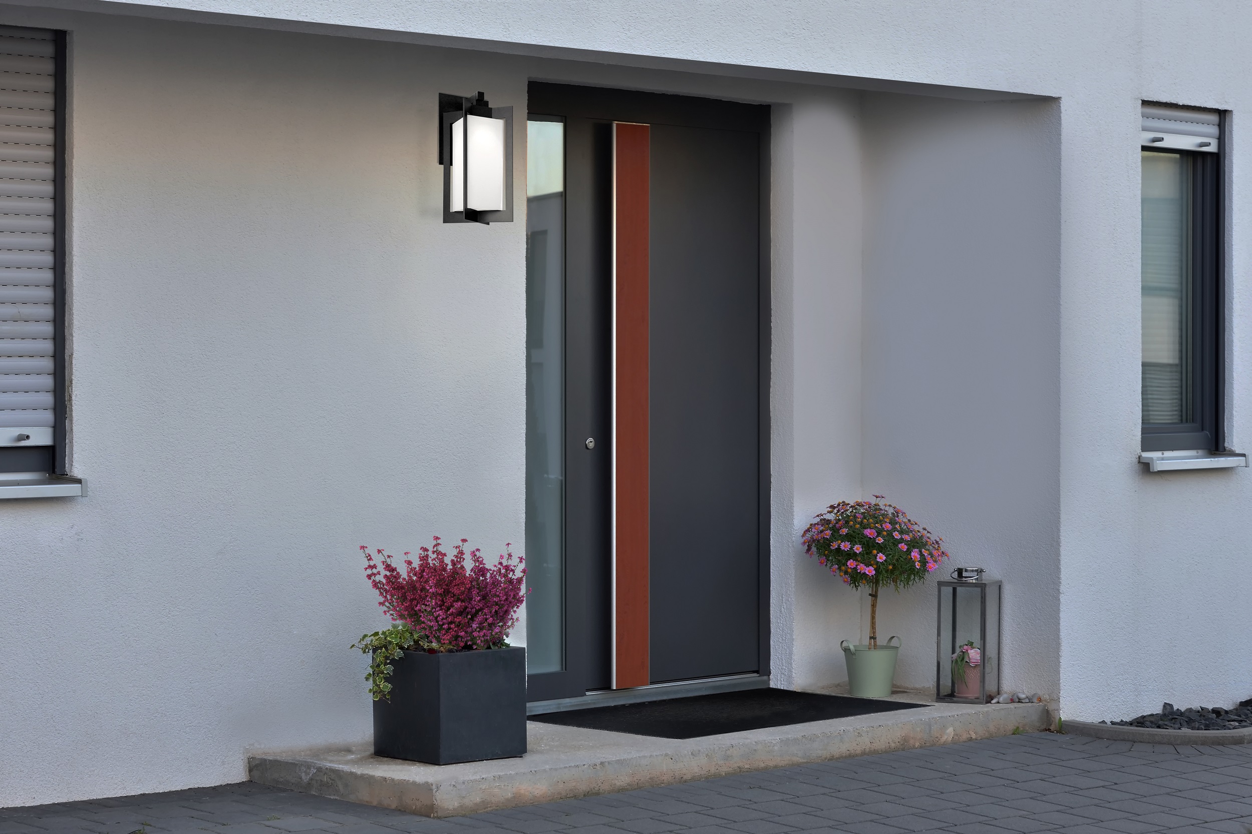 A large gray pot with a green bush in front of the entrance to the house next to the front gray door.