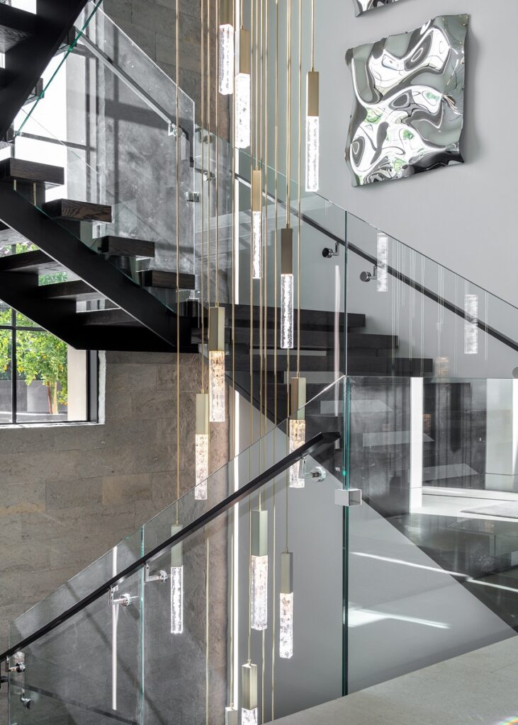 A custom Hammerton Studio Axis multiport chandelier commands attention in the multi-story stairwell, creating a dazzling three-story display of light.